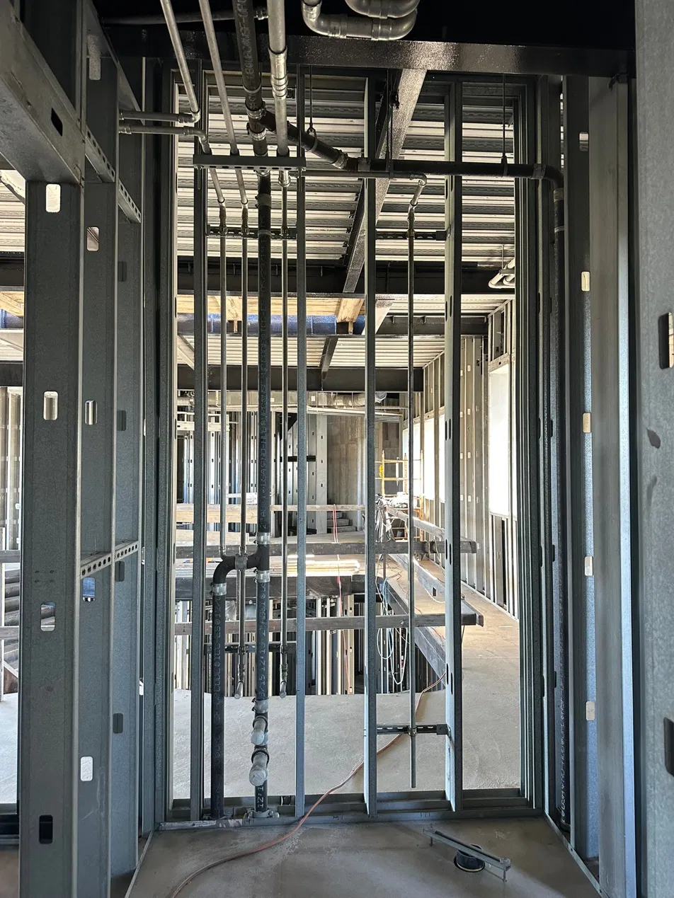 Commercial job site corridor with steel stud framing and overhead plumbing rough-in visible