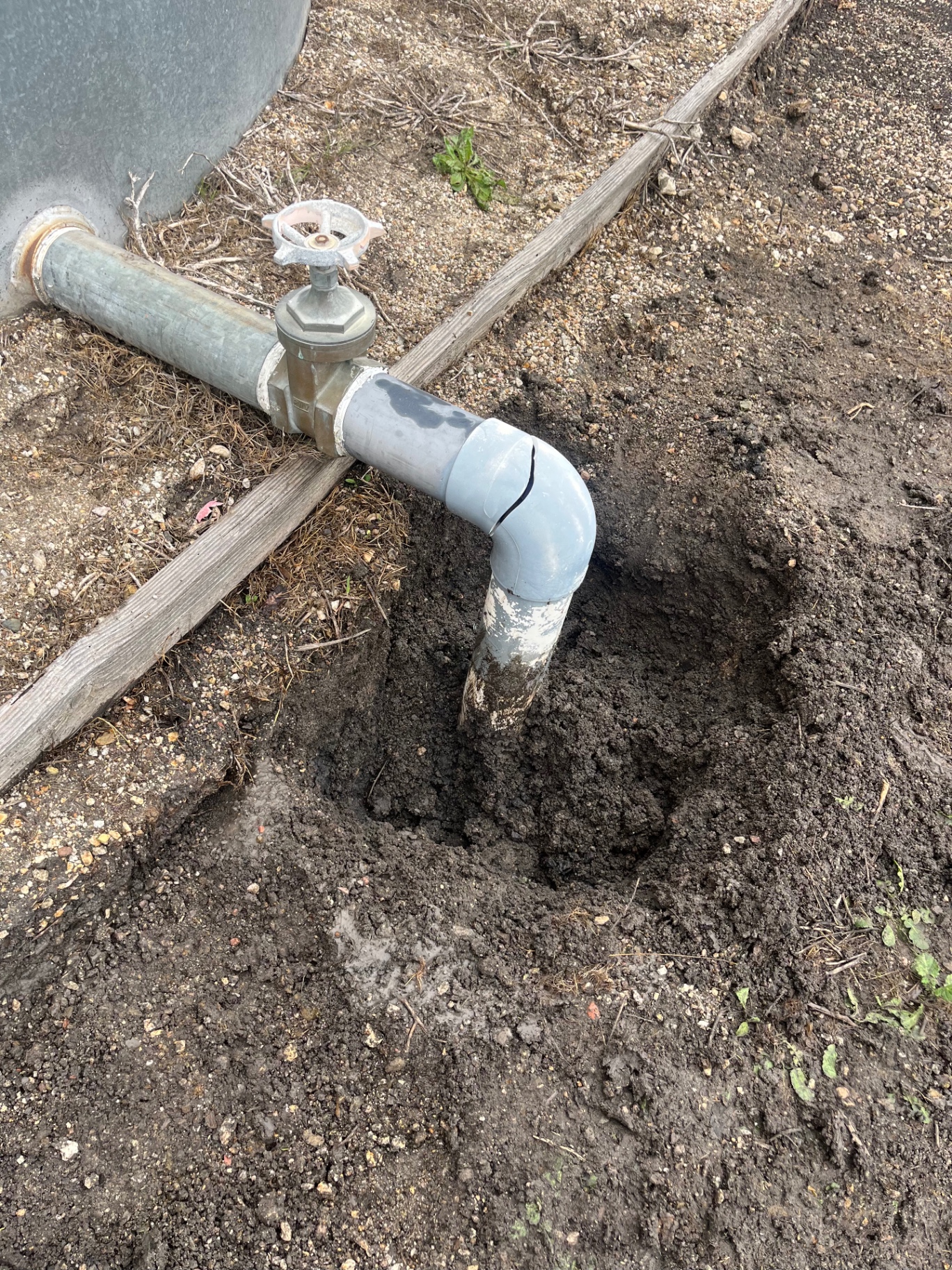 Excavated cracked PVC pipe with valve, showing an active leak repair in progress