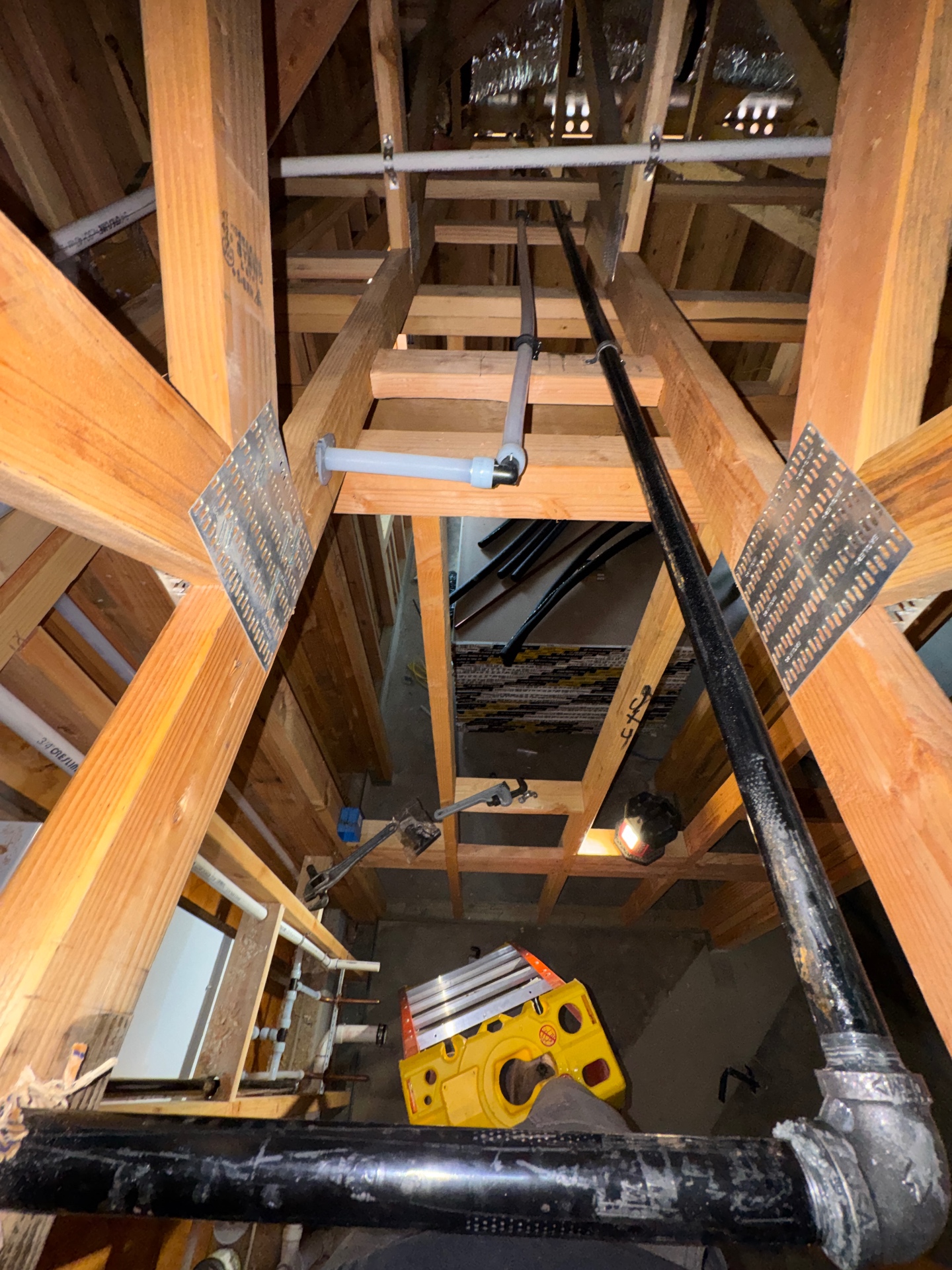 Black iron gas pipe running through wood framing in an attic